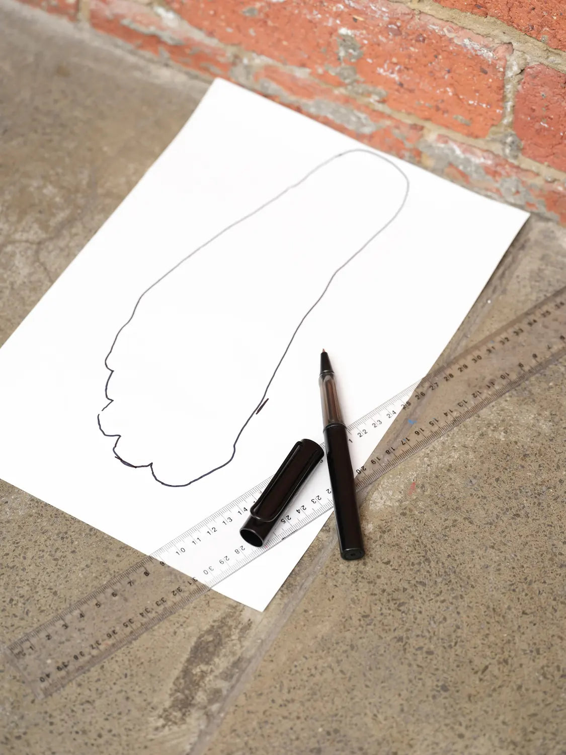 Outline of a feet on paper with a pen and ruler on a concrete surface.