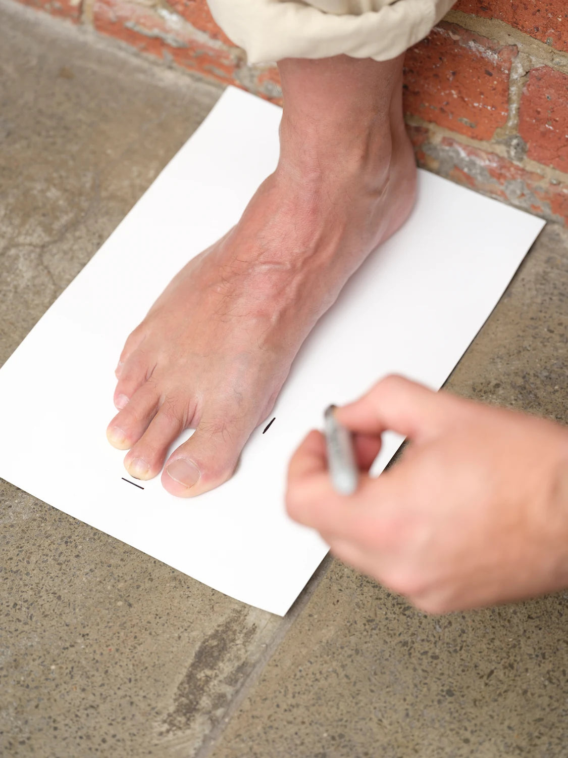Person taking a foot measurement on a white sheet of paper with a pen.