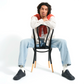 Man wearing black barefoot sneakers seated in a relaxed studio setting