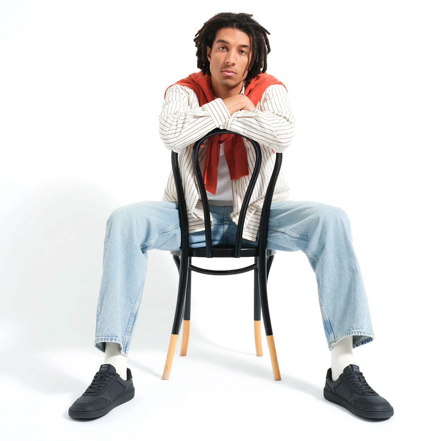 Man wearing black barefoot sneakers seated in a relaxed studio setting
